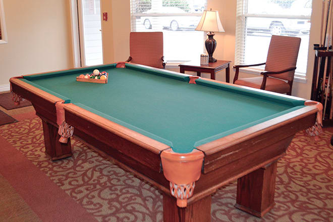 A billiard table set up in a cozy game room with chairs and a lamp.