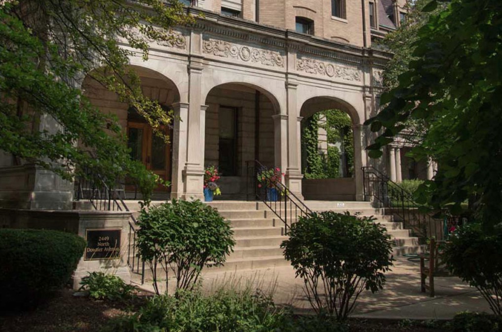 A historic building entrance with columns and greenery.
