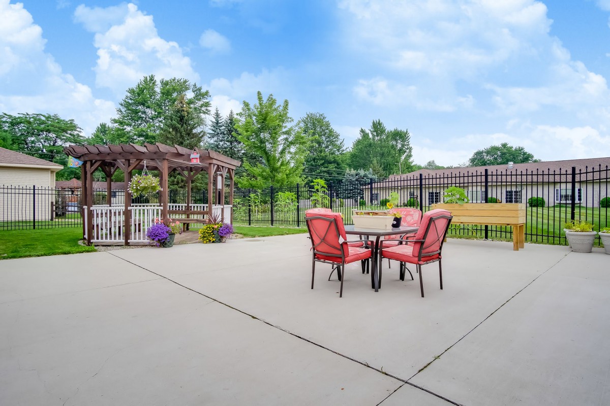 A spacious patio with red outdoor furniture, a pergola, and landscaped surroundings.