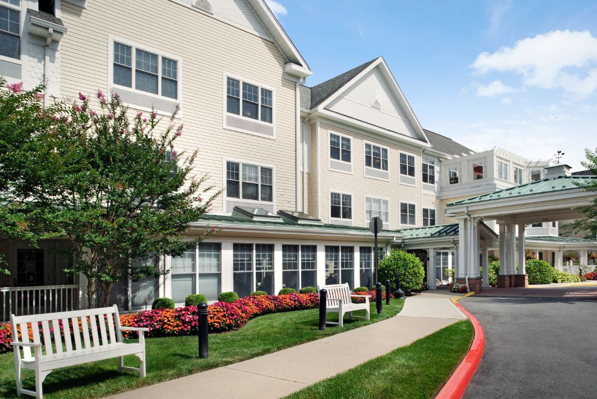 A large residential building with a landscaped garden and benches in the foreground.