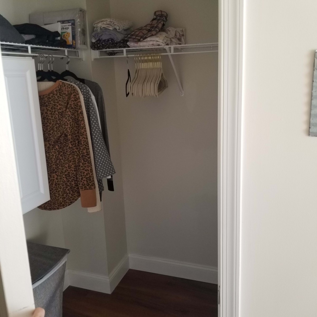 A small closet with clothes hanging on a rack and storage items on the shelves.