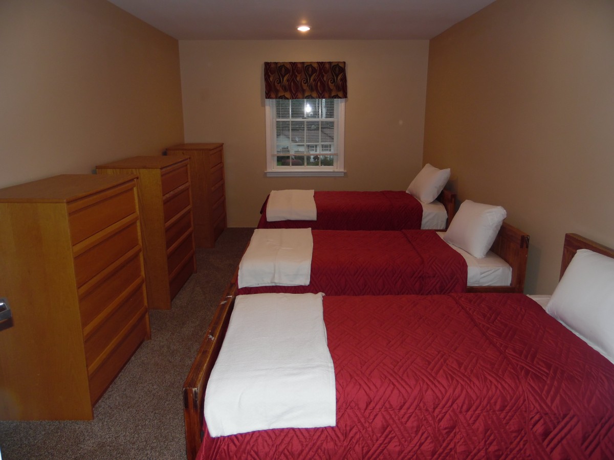 A bedroom with three single beds, red bedding, and two wooden dressers.