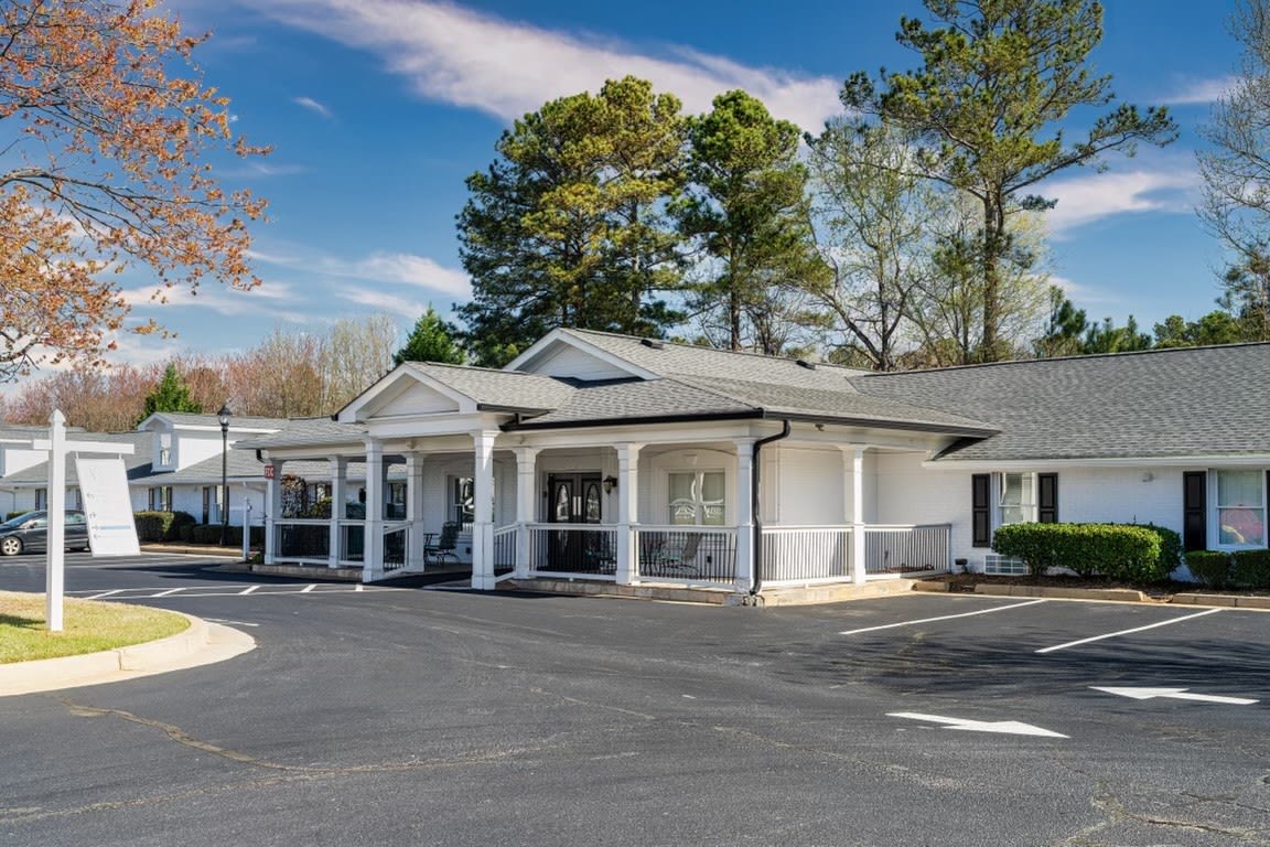 A commercial building with a large parking area and trees in the background.