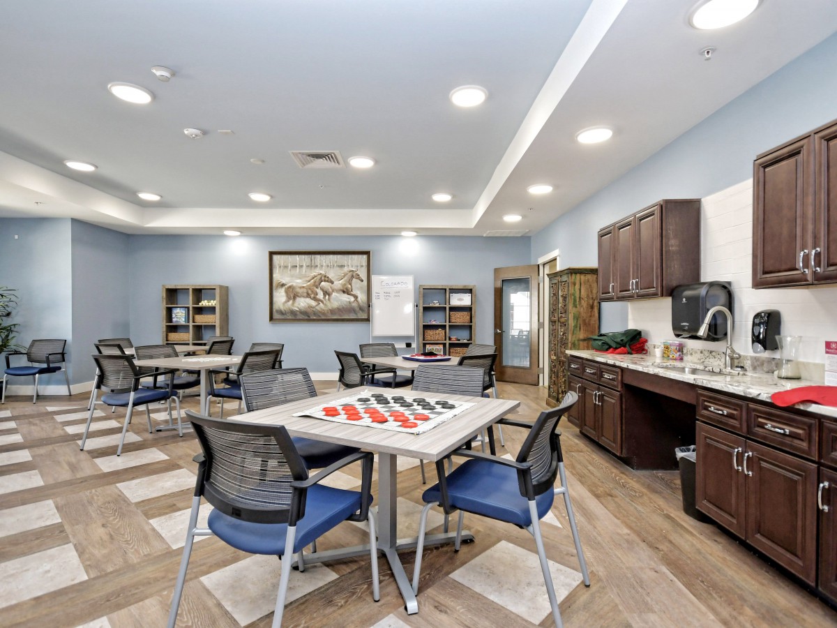 A modern meeting room with tables, chairs, bookshelves, and a coffee station.