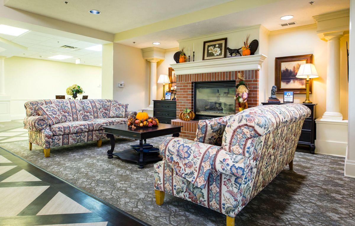 A cozy living room featuring patterned sofas, a central coffee table, and a brick fireplace adorned with decorative items.