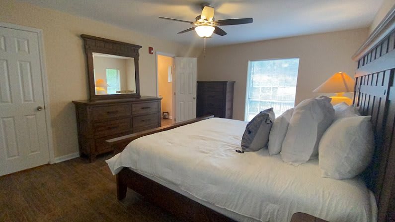 A cozy bedroom featuring a large bed with pillows, a wooden dresser with a mirror, and a ceiling fan.