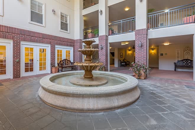 A serene indoor courtyard featuring a central fountain surrounded by benches and plants.