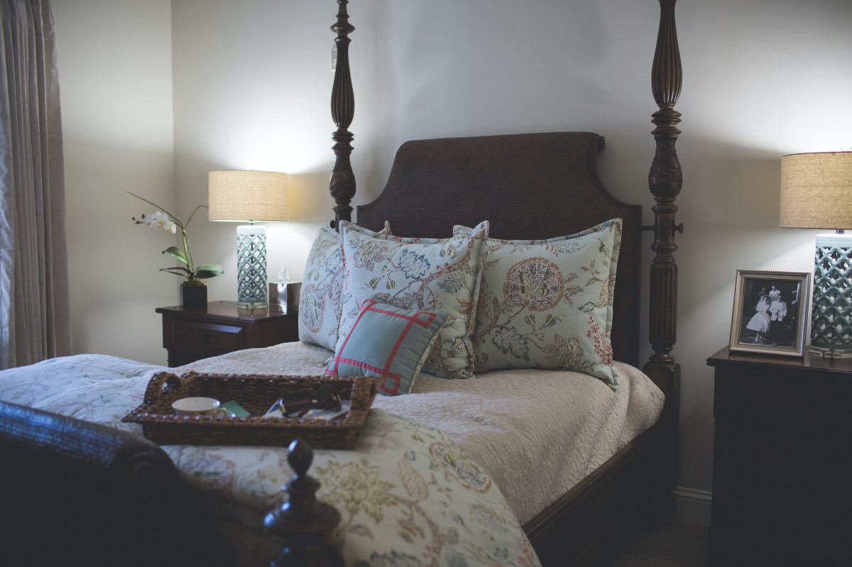A cozy bedroom featuring a four-poster bed adorned with decorative pillows and a bedside lamp on the nightstand.