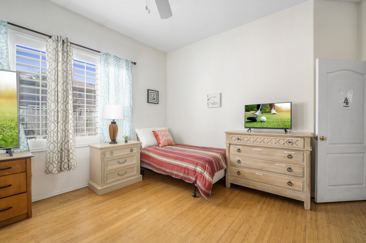 A cozy bedroom featuring a single bed, dresser, and TV with minimalist decor.
