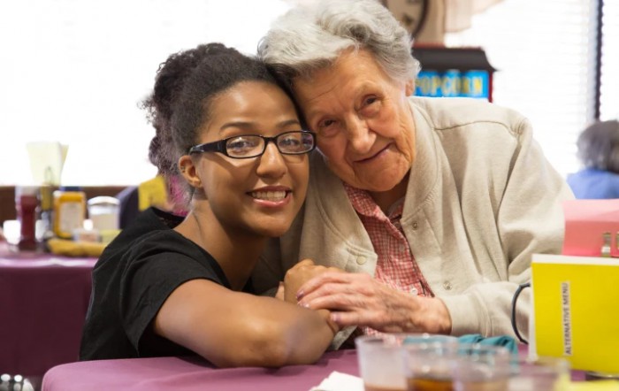 A young woman and an elderly woman smiling and posing together indoors.