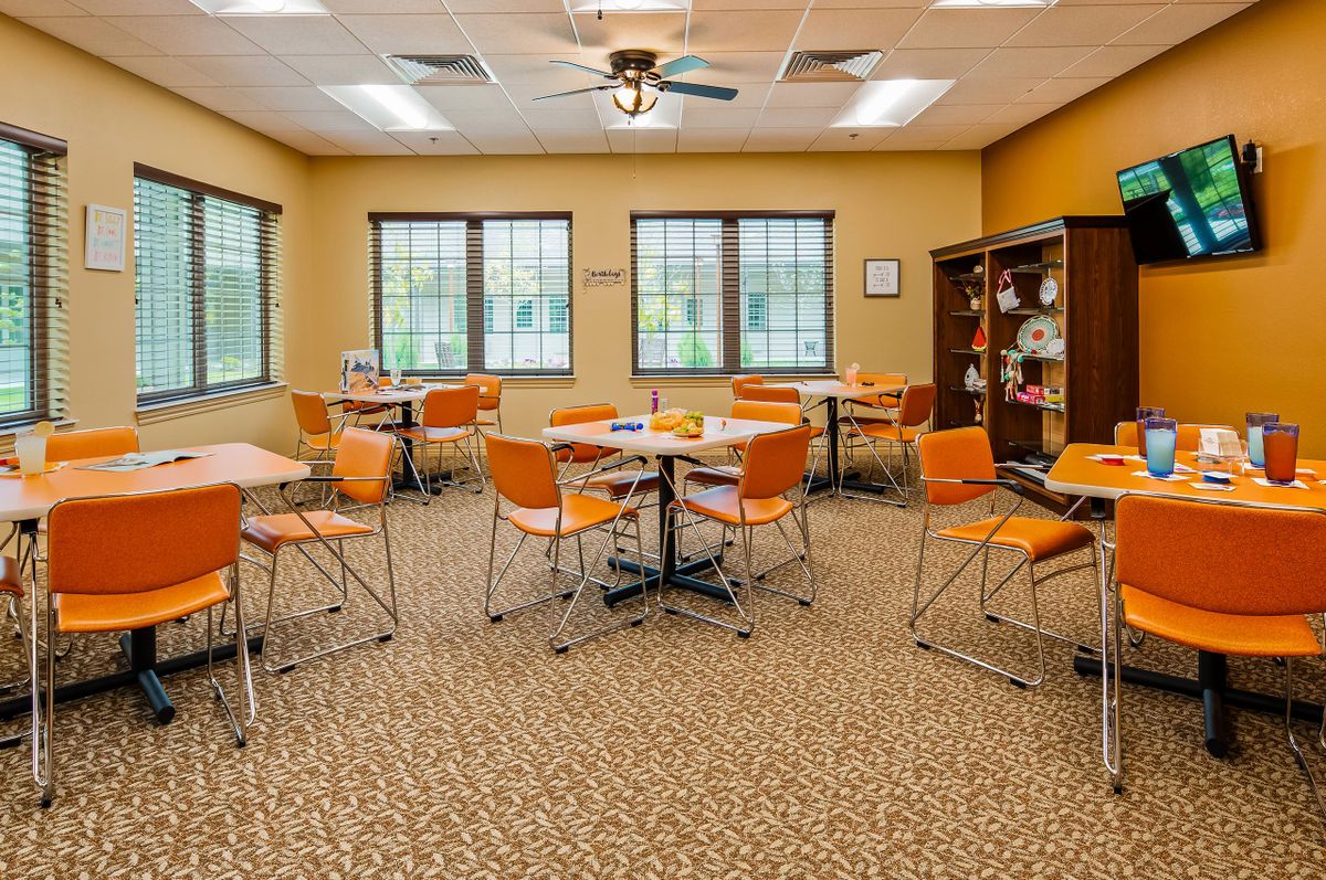 A classroom interior with orange chairs and tables arranged neatly, featuring large windows and a beige color scheme.