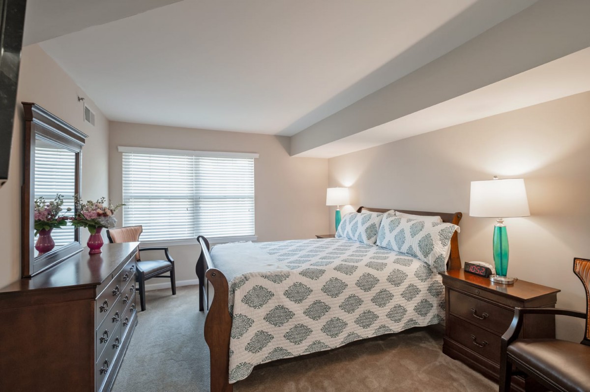 A cozy bedroom with a stylish bed, two lamps, and a large window letting in natural light.