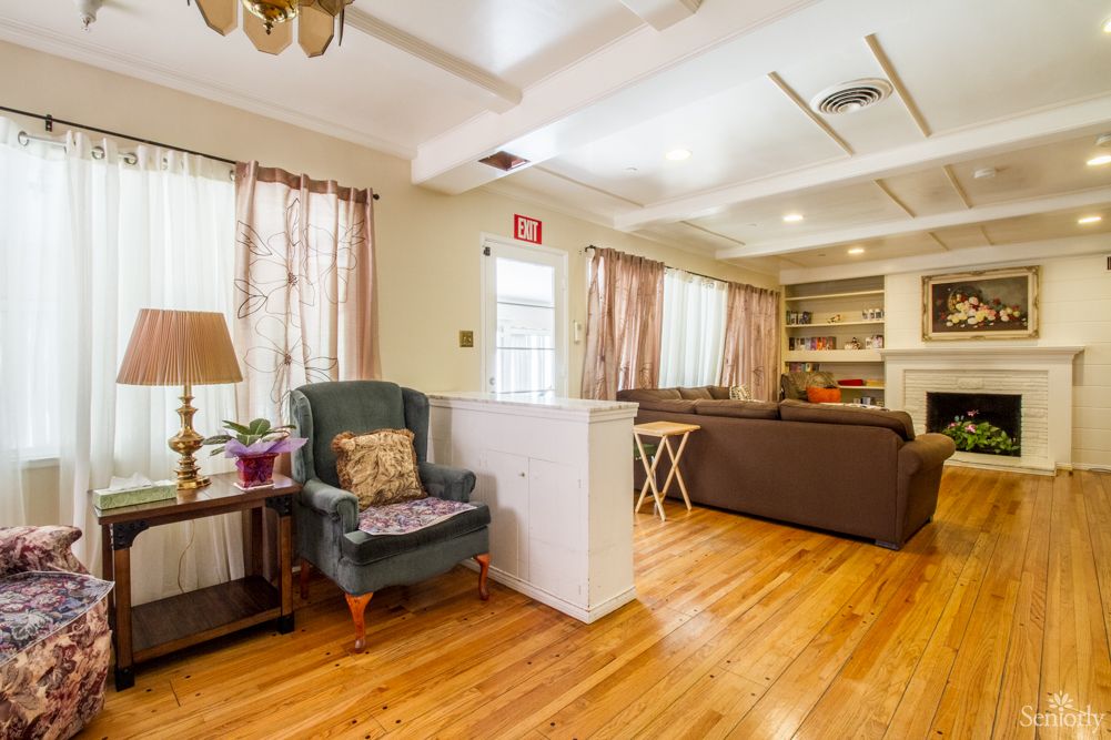 A cozy living room with hardwood floors, featuring a sofa, armchair, and a fireplace.