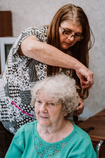 A caregiver styles the hair of an elderly woman in a warm and caring environment.