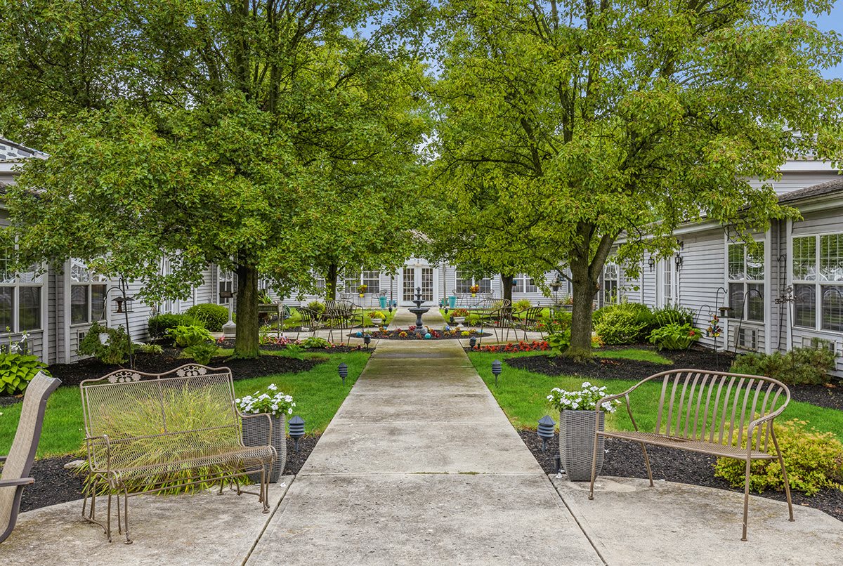A scenic garden pathway leading towards a white building, surrounded by lush greenery and trees.