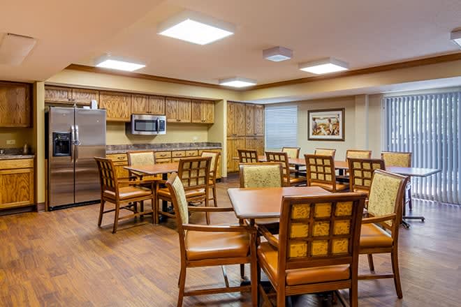 A well-lit dining area with wooden furniture and a kitchen setup.