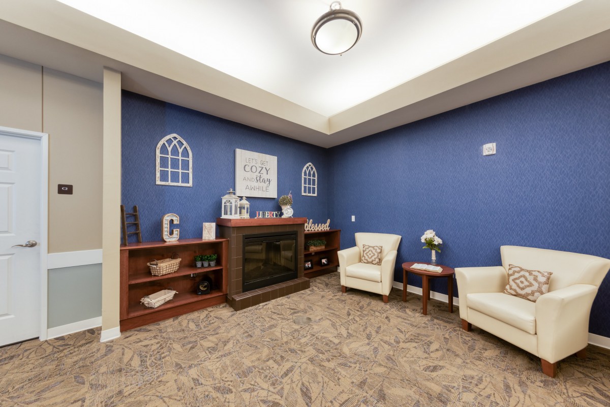 A cozy living room with blue walls, featuring armchairs and a fireplace alongside decorative bookshelves.