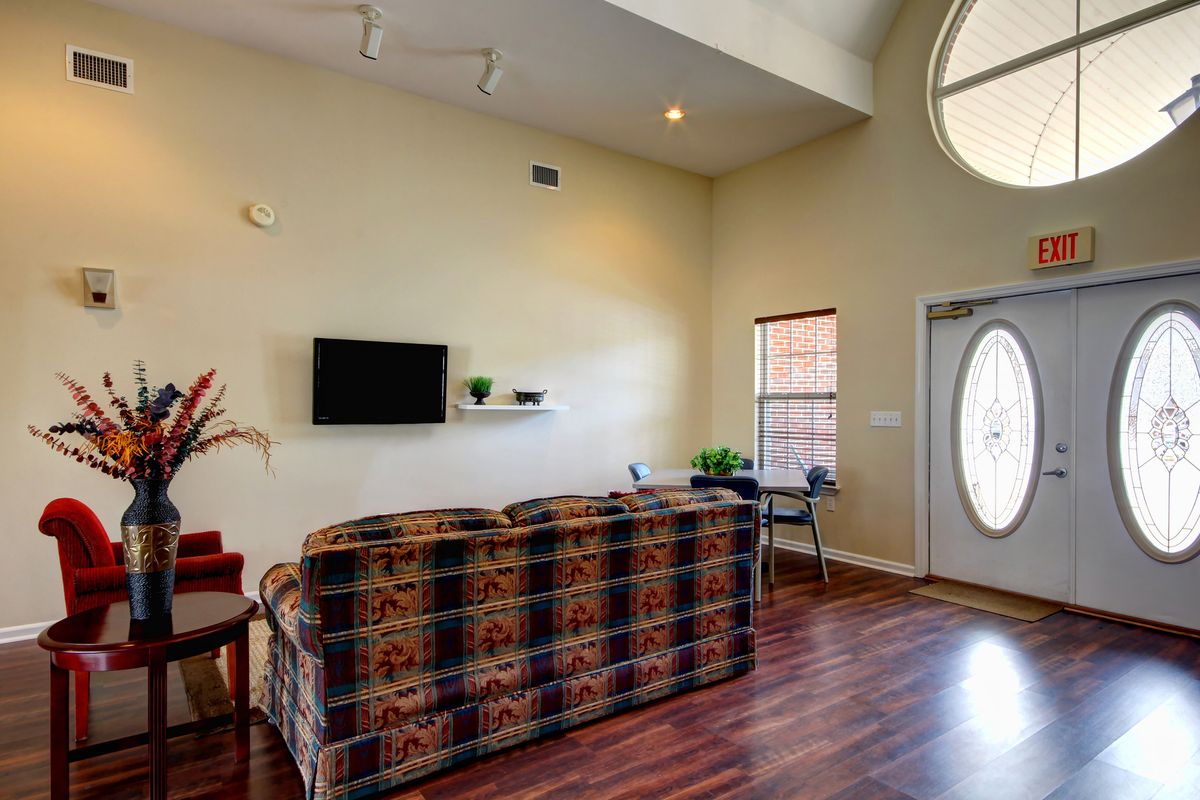 A cozy living room with a patterned sofa, wall-mounted television, and wood flooring.