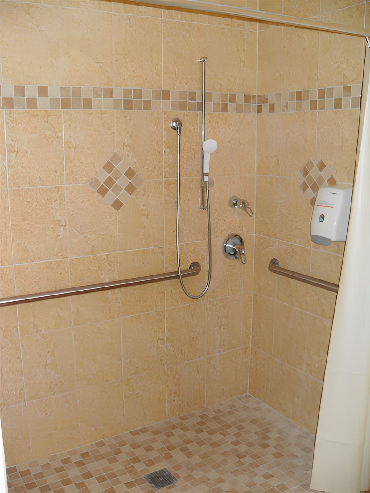 A tiled bathroom shower with safety grab bars and a handheld showerhead.