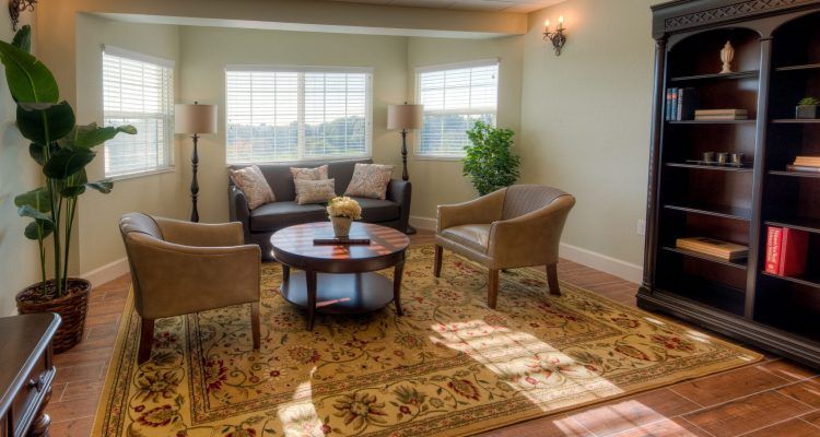 A cozy living room with a sofa, chairs, and a coffee table, illuminated by natural light.