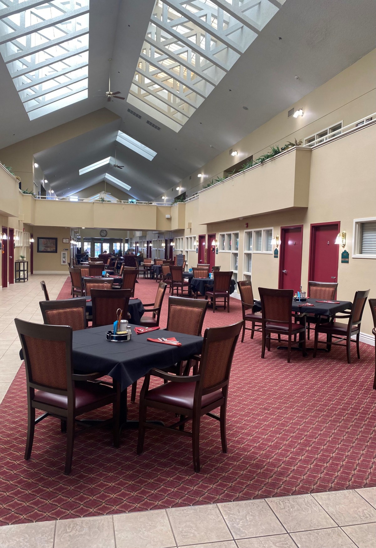 A spacious indoor dining area with multiple tables and chairs, featuring skylights and a carpeted floor.