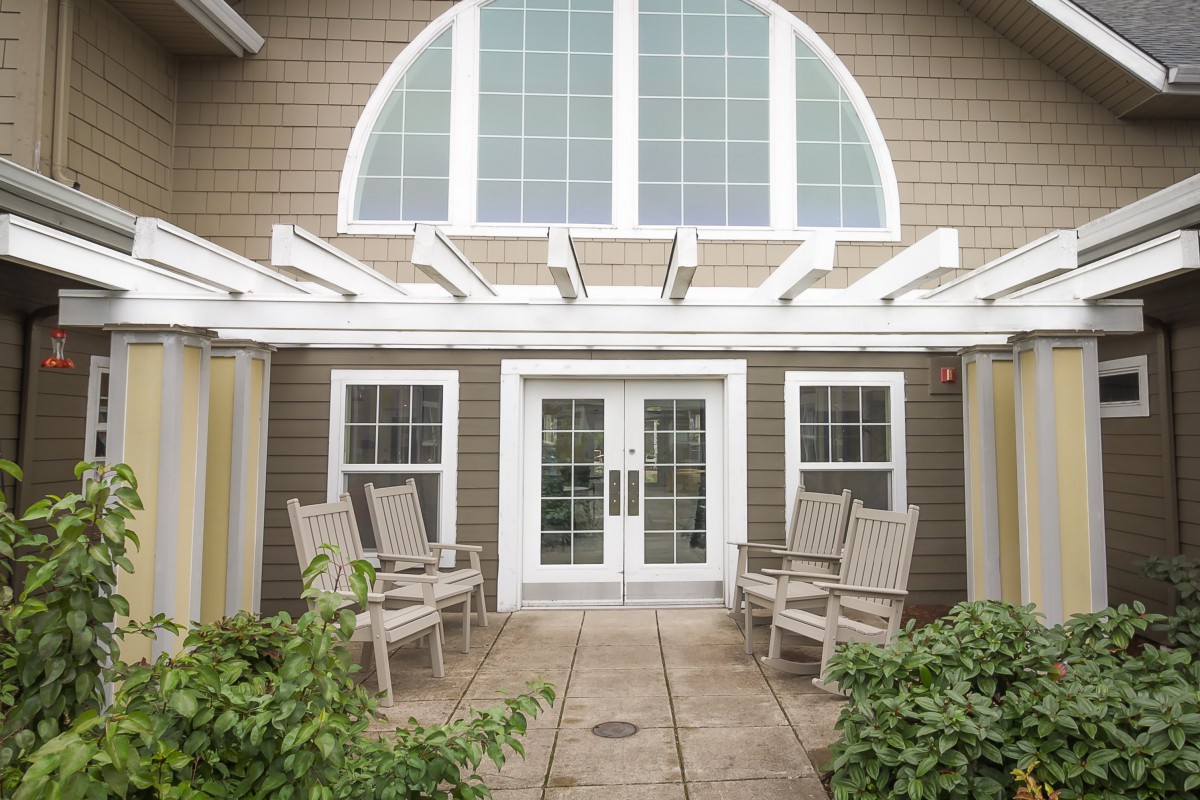 A cozy outdoor patio area with chairs under a pergola, featuring large windows and a double door entrance.