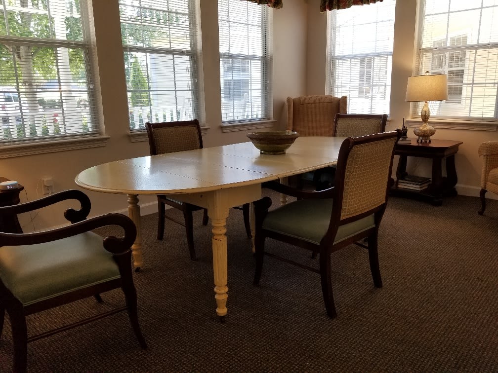 A cozy dining area with a white oval table and upholstered chairs, illuminated by natural light from large windows.
