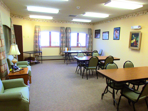 A cozy community room set up with tables and chairs, featuring large windows that bring in natural light.