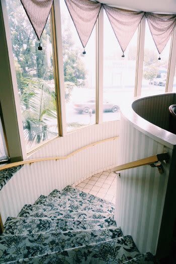 A spiraling staircase with a wooden handrail next to large windows.