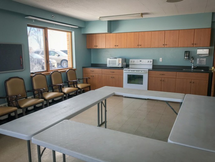 A multi-purpose room featuring a kitchen area with appliances and a U-shaped table setup with chairs.