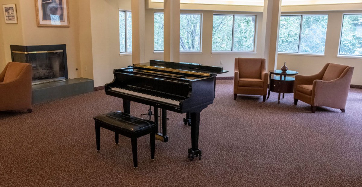 A grand piano in a well-lit music room with comfortable seating.