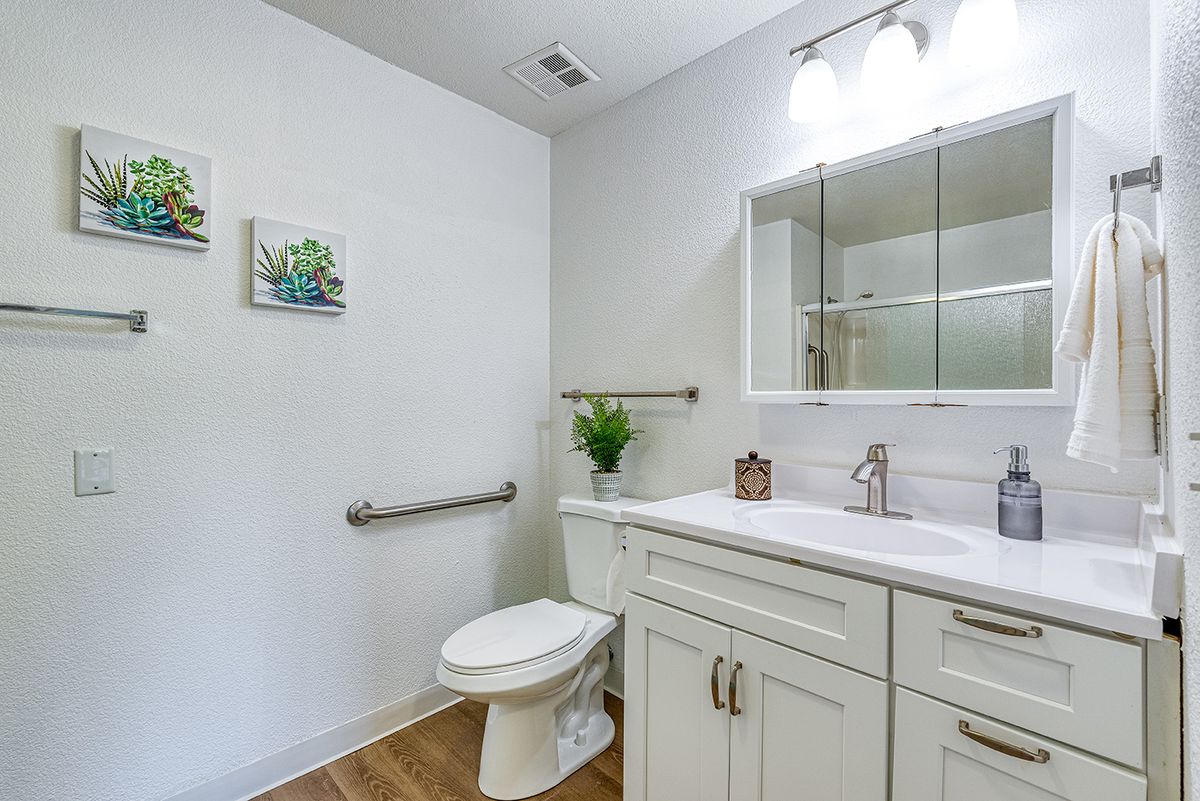 A modern bathroom with a white vanity, toilet, and mirror under bright lighting.