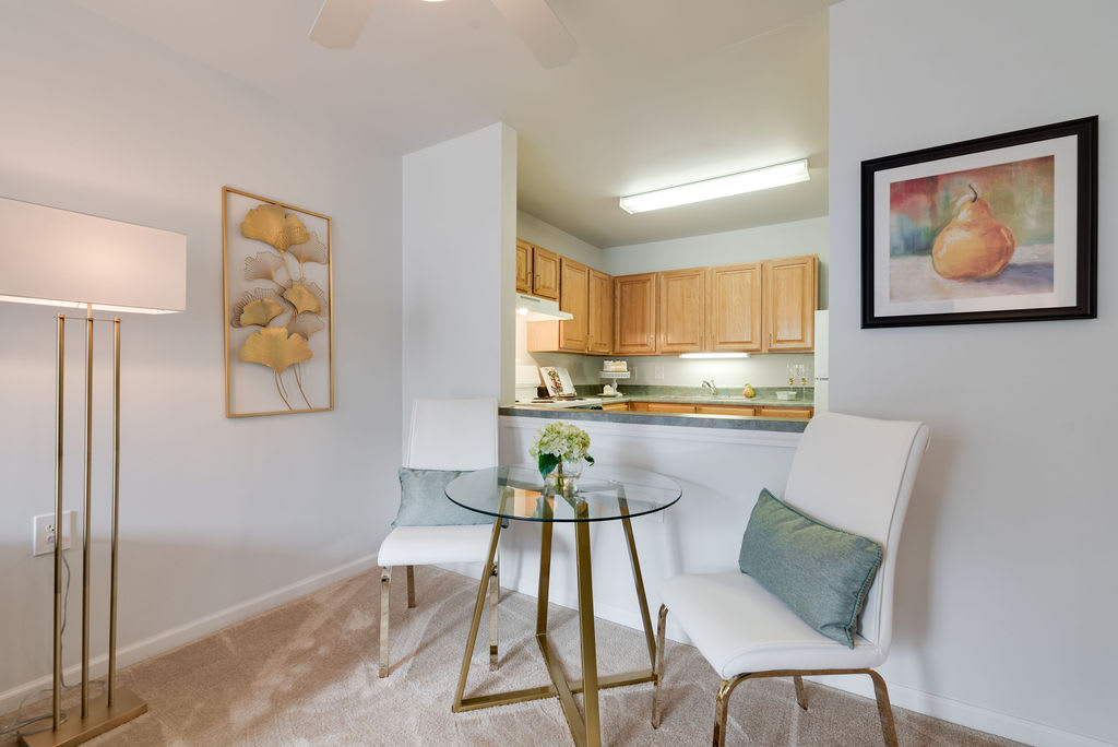 A cozy dining area with a glass table and two white chairs, adjacent to a modern kitchen.