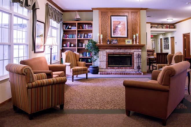 A cozy living room with a fireplace and comfortable armchairs, surrounded by bookshelves.