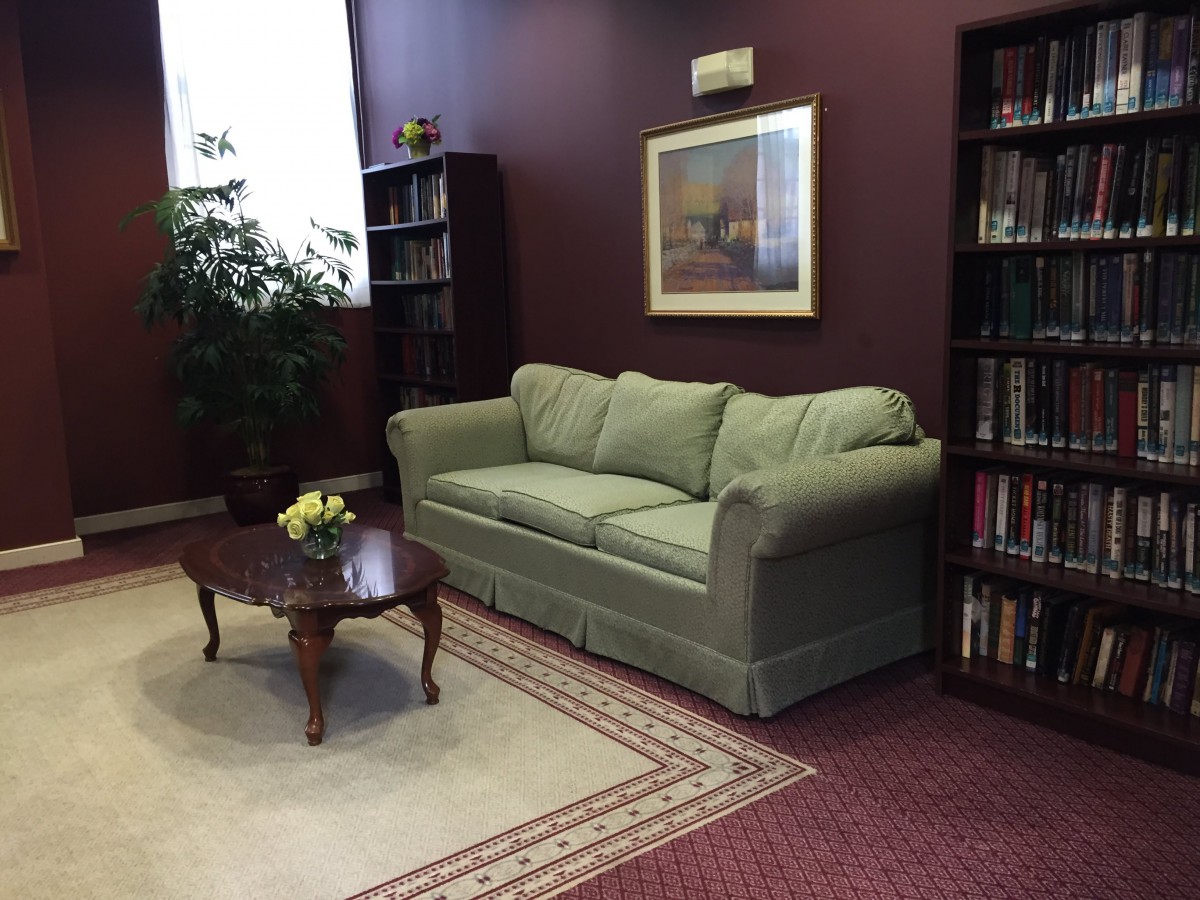 A cozy living room with a green sofa, a coffee table with flowers, bookshelves, and a decorative rug.