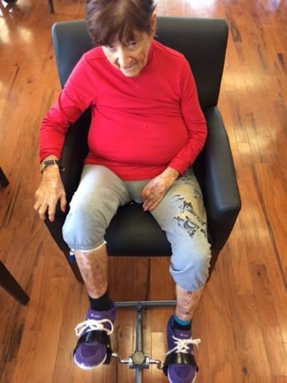 An elderly person wearing a red shirt sits in an armchair on a wooden floor.