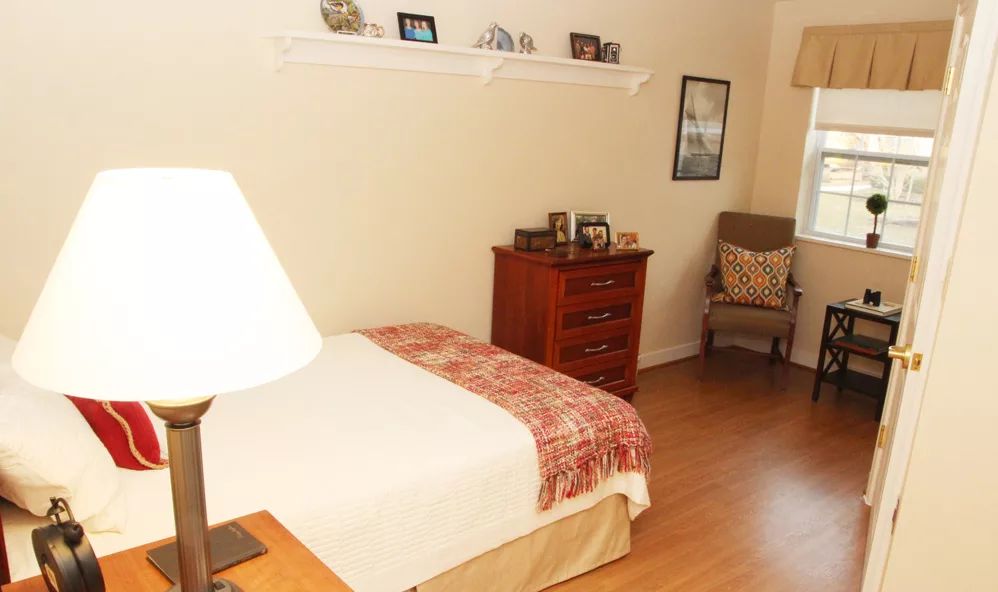 A cozy bedroom with a bed, dresser, and chair, featuring warm decor.