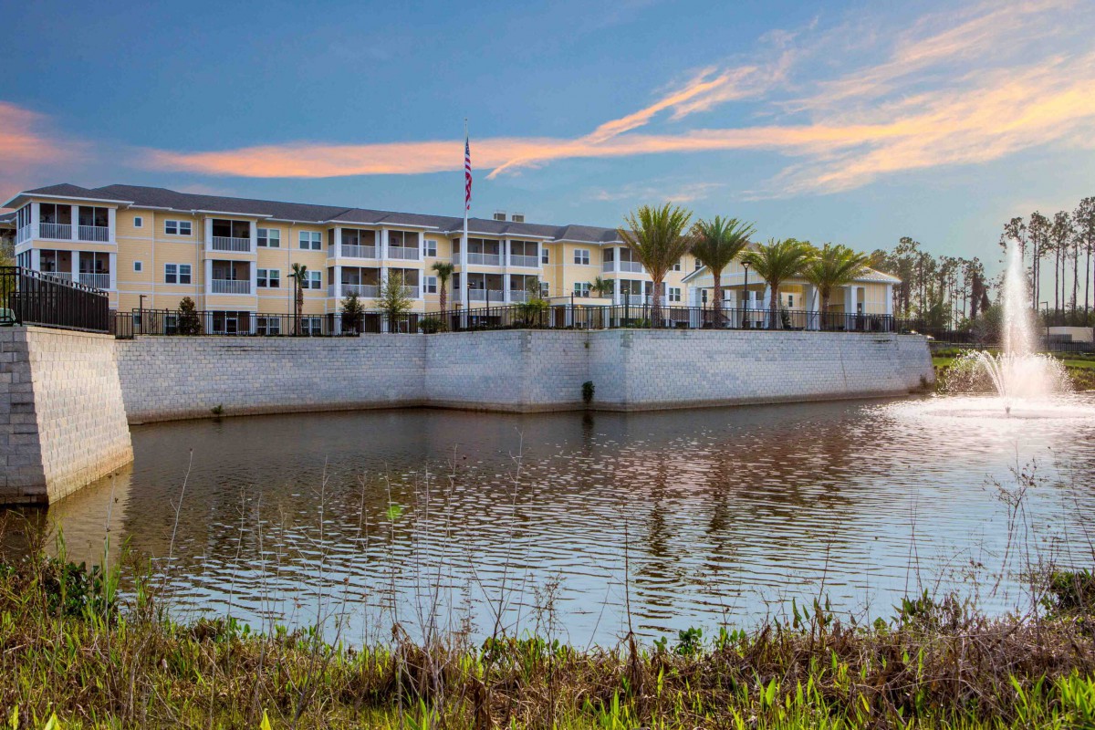 A modern building with palm trees reflected in a nearby body of water under a colorful sky.