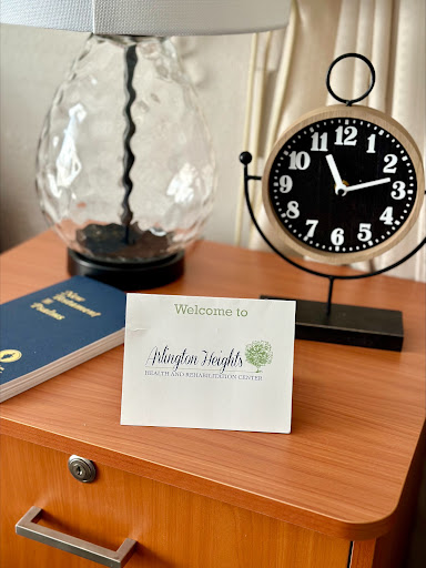 A cozy setup featuring a decorative lamp, a stylish clock, and a welcome note on a wooden table.