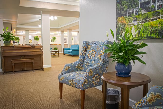 A cozy lobby area featuring a patterned chair, potted plant, and piano in the background.