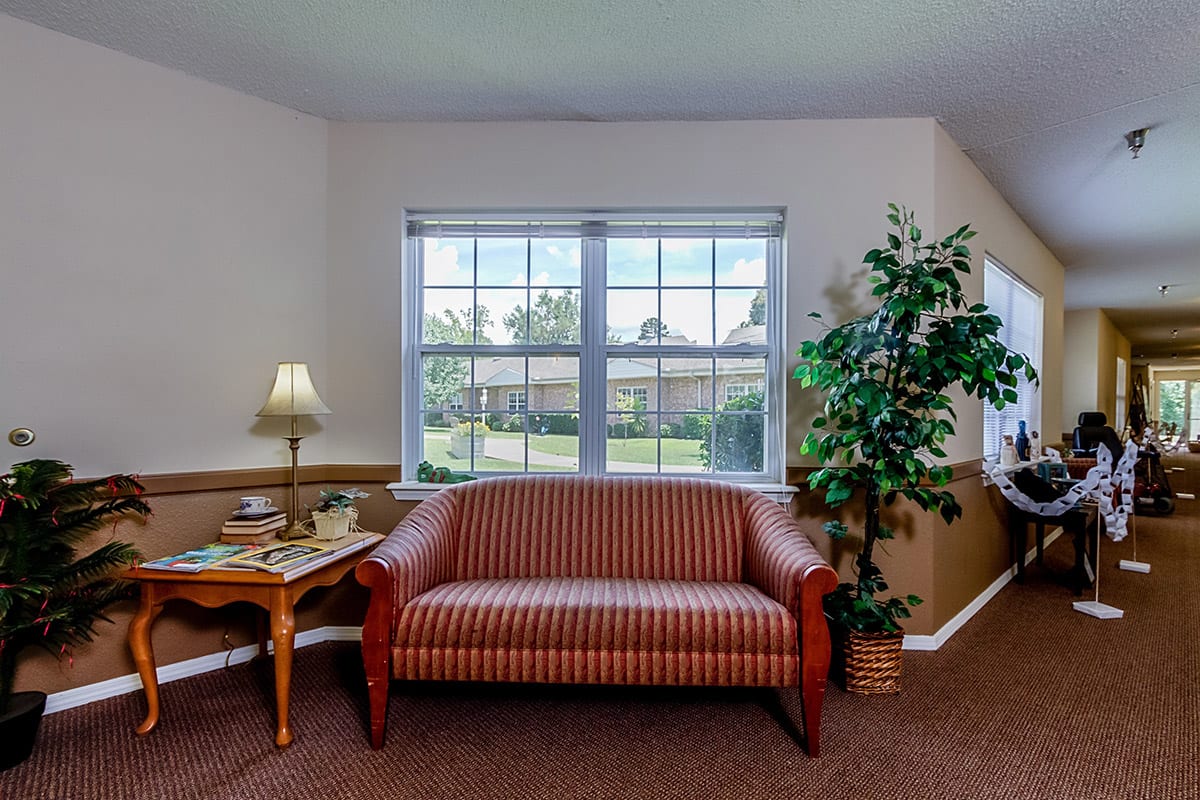 A cozy living room setup with a sofa under a large window, accompanied by a lamp on a wooden table and an indoor plant.