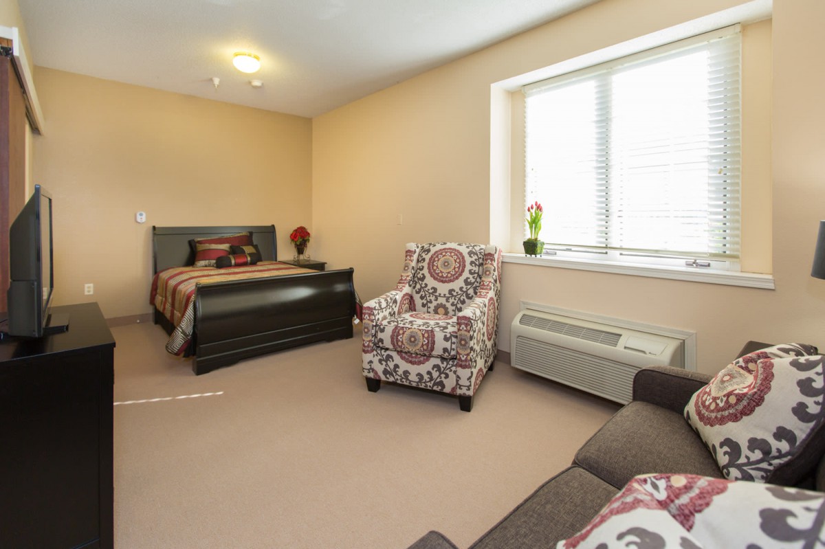 A cozy bedroom featuring a bed, patterned armchair, and window with natural light.