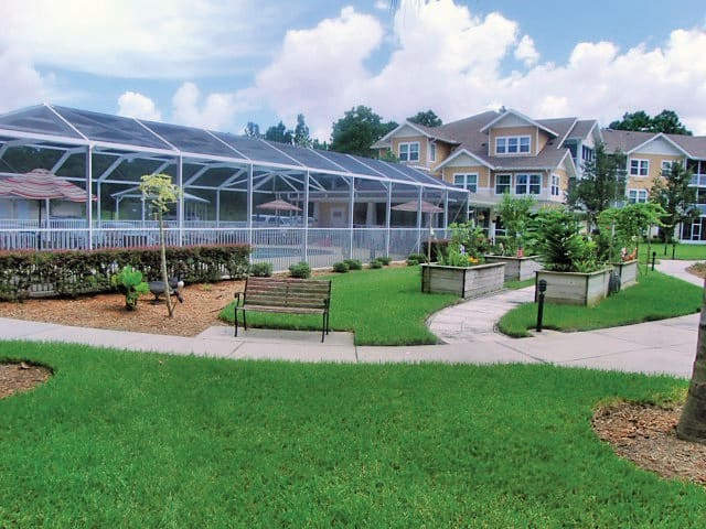 A scenic backyard with a greenhouse, well-maintained garden, and comfortable benches leading to a large house.