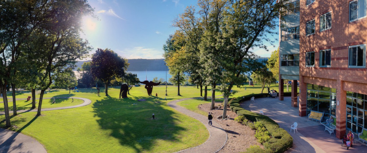 A serene park with sculptures, surrounded by trees and overlooking a picturesque lake on a sunny day.