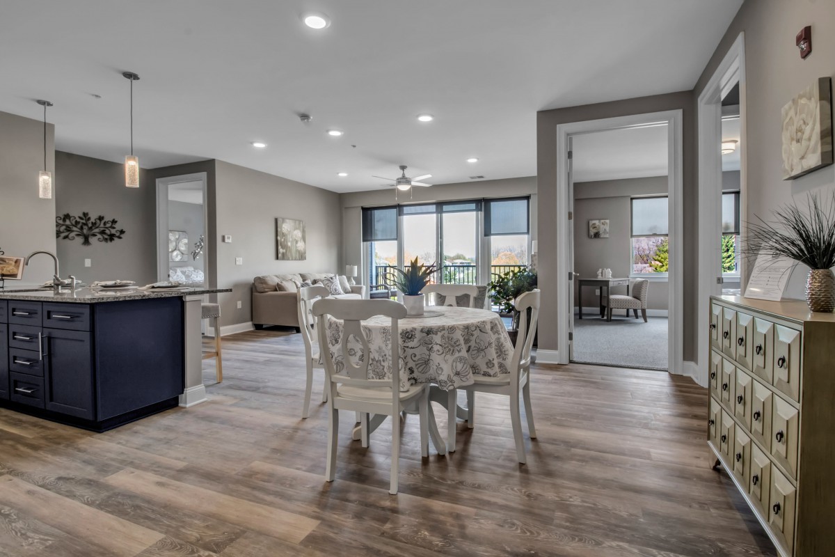 A modern dining area with an open layout, featuring wooden flooring and ample natural light.