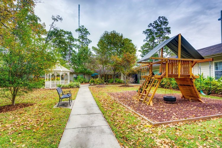 A scenic outdoor playground area with a gazebo, surrounded by trees and a pathway.