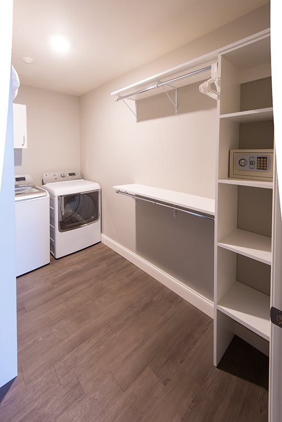 A spacious laundry room with a washer, dryer, shelving, and a closet rod for hanging clothes.