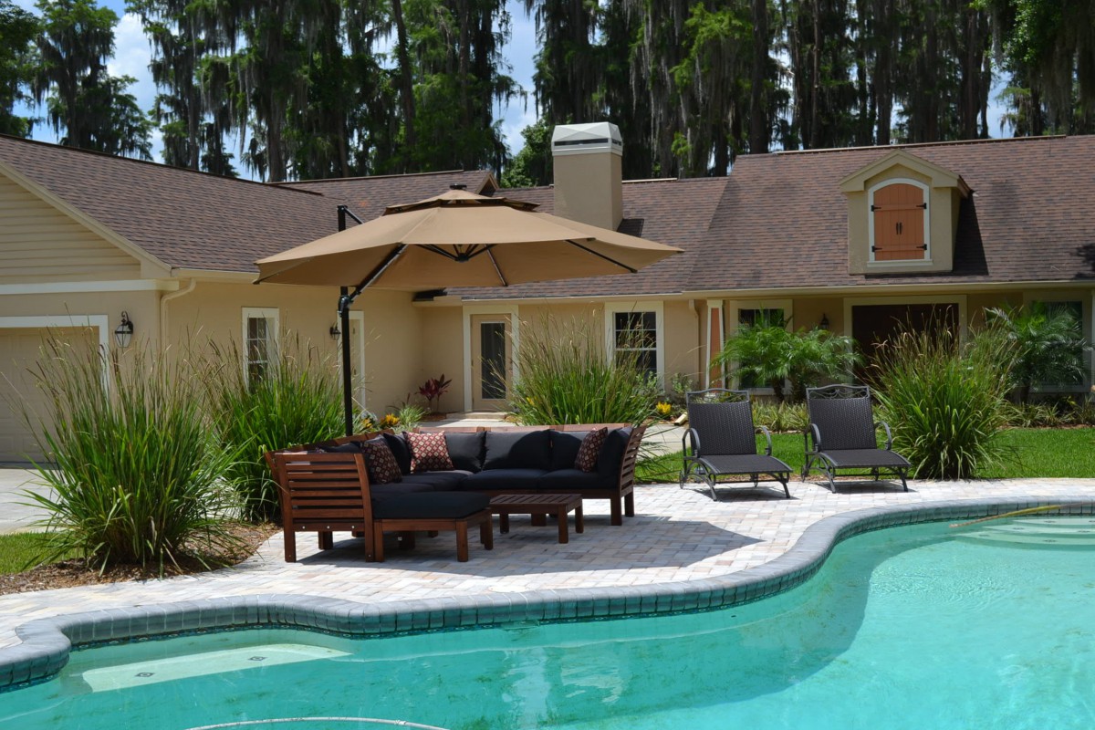A serene backyard with a swimming pool, patio furniture, and an umbrella for shade.