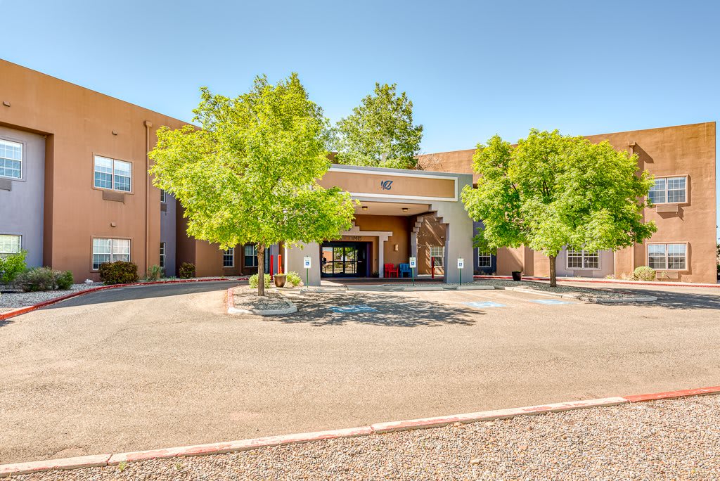 The entrance of a school building surrounded by trees on a sunny day.