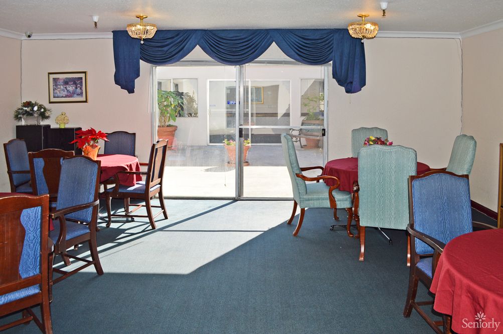 A brightly lit dining area with tables and chairs, featuring blue curtains and a carpeted floor.